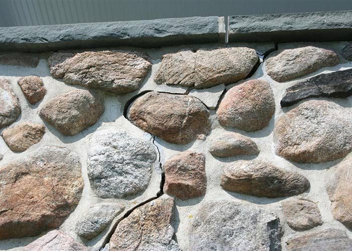 Cracked stone foundation wall showing vertical and horizontal mortar separation.