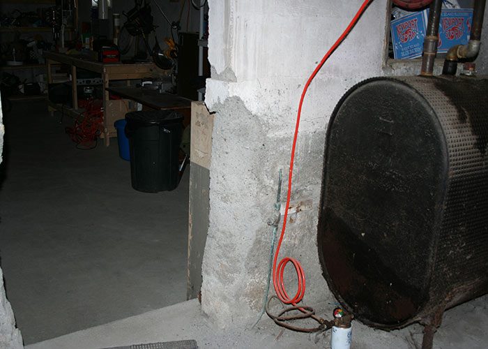Basement foundation column showing cracking and surface deterioration near an oil tank.