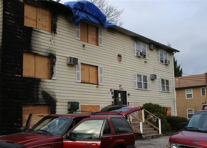 “Multi-unit residential building showing exterior fire damage and boarded openings following a fire event.