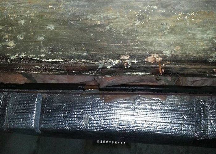 Deteriorated floor framing with moisture damage and corrosion above insulated ductwork.